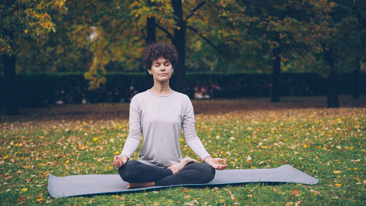 Woman meditating peacefully on a yoga mat outdoors.