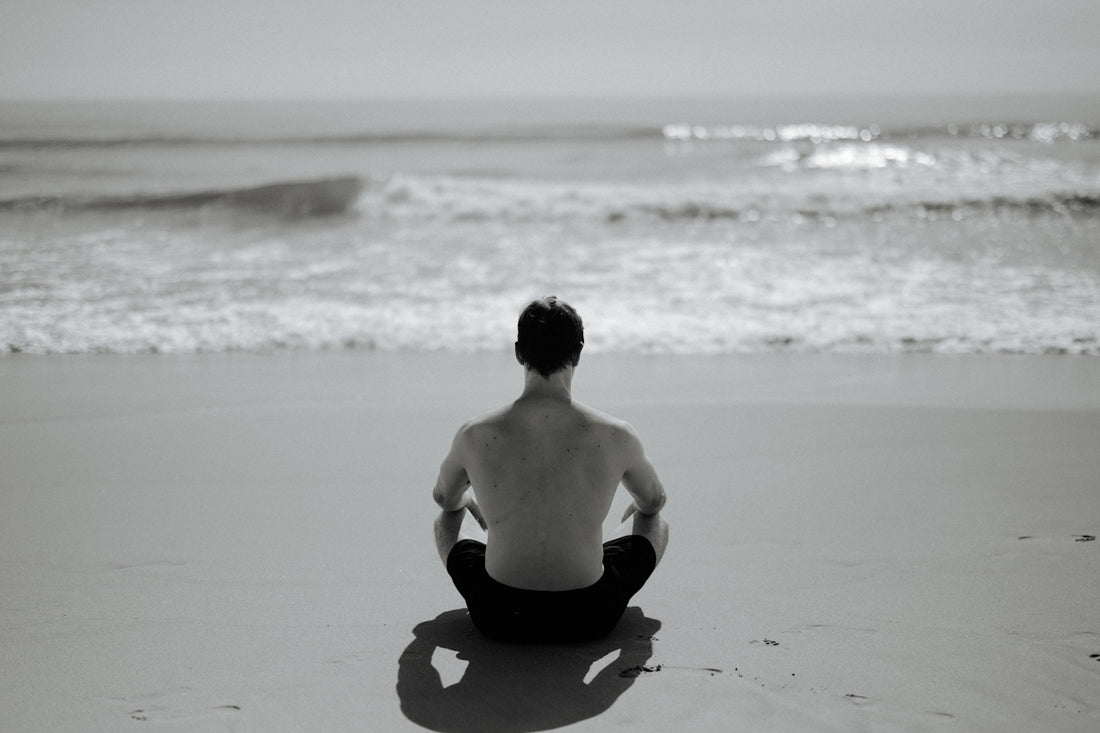 Man meditating on a beach facing the ocean