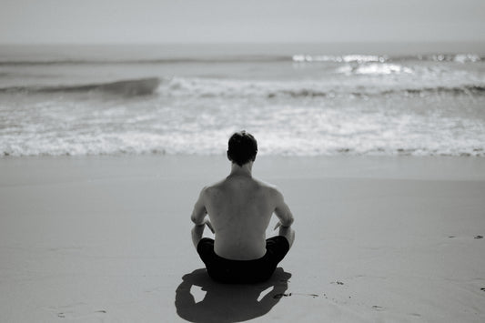 Man meditating on a beach facing the ocean